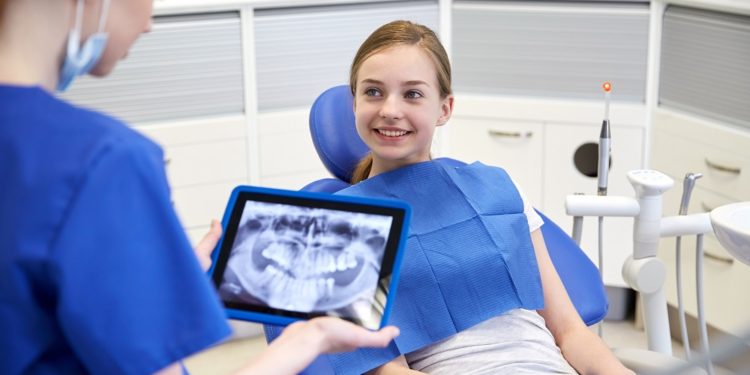 people, medicine, stomatology, technology and health care concept - happy female dentist with teeth x-ray on tablet pc computer and patient girl at dental clinic office