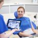 people, medicine, stomatology, technology and health care concept - happy female dentist with teeth x-ray on tablet pc computer and patient girl at dental clinic office