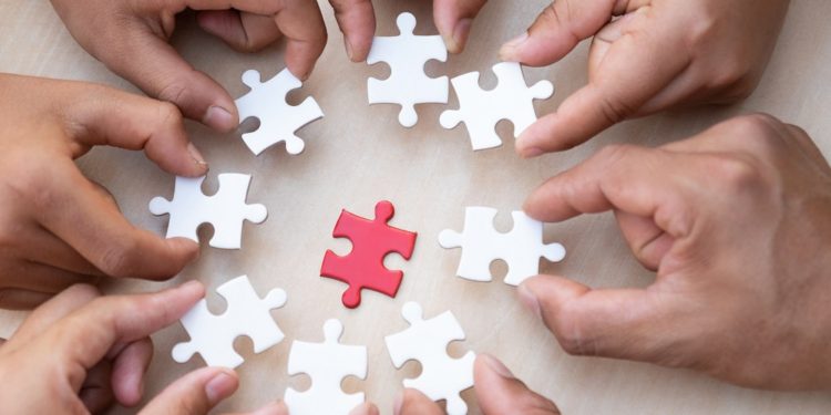 Hands holding piece of blank jigsaw puzzle with wooden table background.