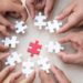 Hands holding piece of blank jigsaw puzzle with wooden table background.