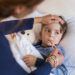 Sick boy with thermometer laying in bed and mother hand taking temperature. Mother checking temperature of her sick son who has thermometer in his mouth. Sick child with fever and illness while resting in bed.