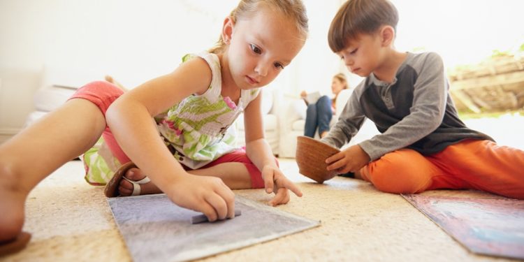 Little boy and girl coloring pictures with chalk colors while sitting on floor in living room at home.