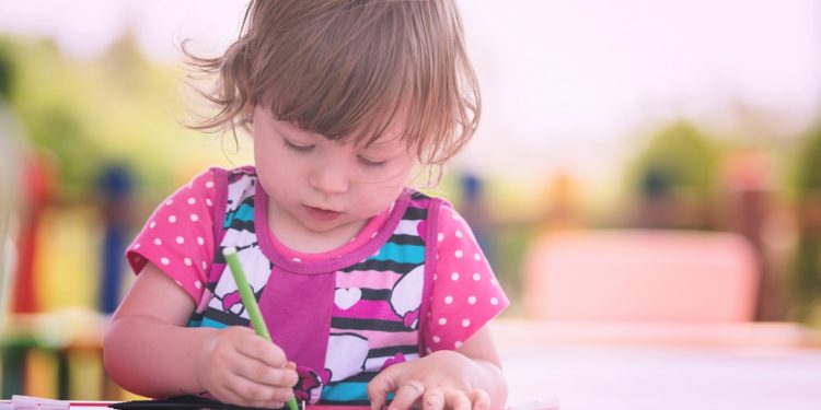 cute little girl cheerfully spending time using pencil crayons while drawing a colorful pictures in the outside playschool