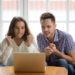 Nervous excited couple in tension clenching fists looking at laptop screen, man and woman football fans cheering supporting sport team watching championship match online together hope for win at home