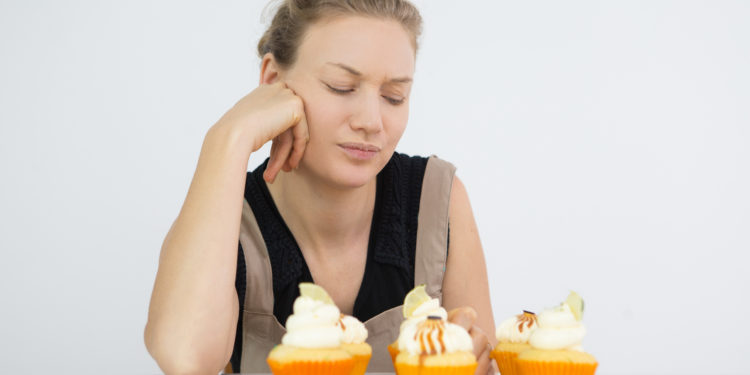 Concentrated young woman thinking of missing ingredient in cupcakes while testing them. Displeased housewife preparing dessert for Halloween. Confectioner concept