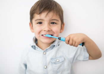 A smiley boy cleans a teeth isolated on grey background