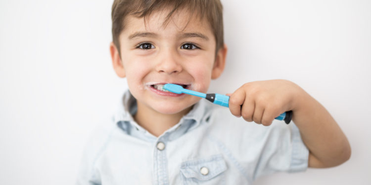 A smiley boy cleans a teeth isolated on grey background