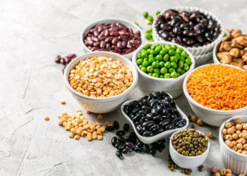 Selection of legumes - beans, lentils, mung, chickpea, pea in white bowls on stone background