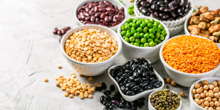 Selection of legumes - beans, lentils, mung, chickpea, pea in white bowls on stone background