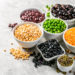 Selection of legumes - beans, lentils, mung, chickpea, pea in white bowls on stone background
