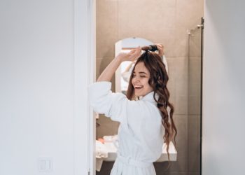 Beautiful smiling woman curling long hair using curling iron in the bath
