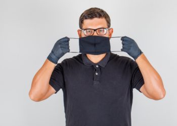 Doctor wearing mask in black polo shirt and looking serious. front view.