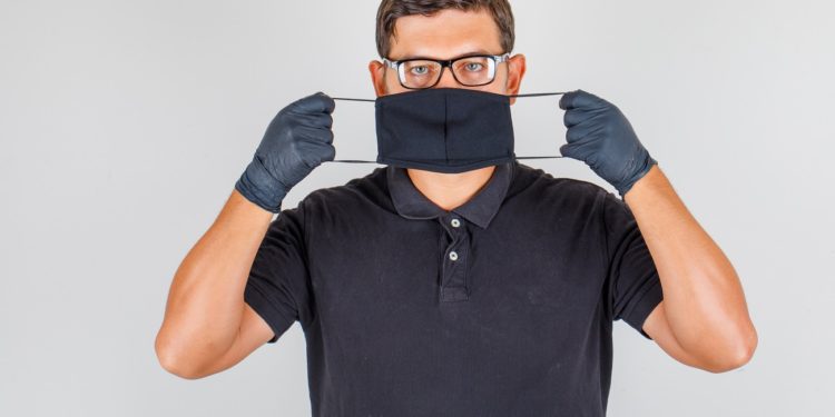 Doctor wearing mask in black polo shirt and looking serious. front view.