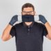 Doctor wearing mask in black polo shirt and looking serious. front view.