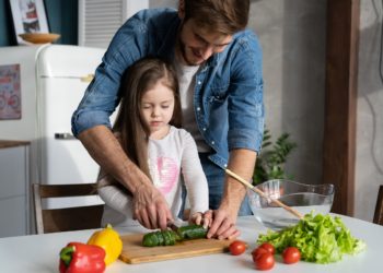 Handsome man and his little cute daughter are cooking on kitchen. Making salad. Healthy lifestyle concept