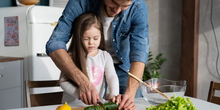 Handsome man and his little cute daughter are cooking on kitchen. Making salad. Healthy lifestyle concept