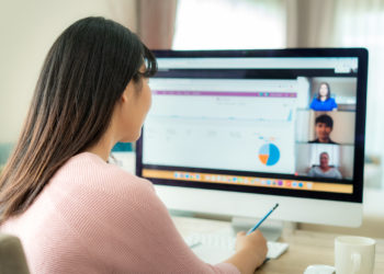 Back view of Asian business woman talking to her colleagues about plan in video conference. Multiethnic business team using computer for a online meeting in video call. Group of people smart working from home.