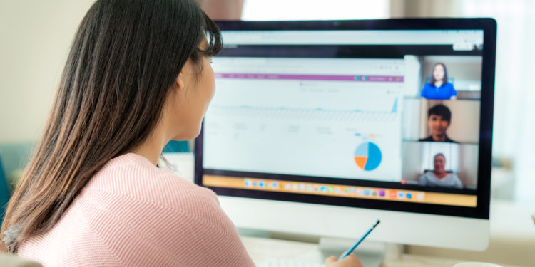 Back view of Asian business woman talking to her colleagues about plan in video conference. Multiethnic business team using computer for a online meeting in video call. Group of people smart working from home.