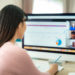 Back view of Asian business woman talking to her colleagues about plan in video conference. Multiethnic business team using computer for a online meeting in video call. Group of people smart working from home.