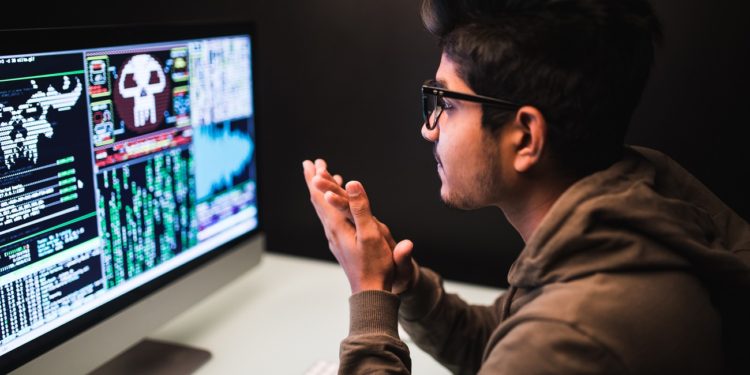 cybercrime, hacking and technology concept - male hacker with smartphone and coding on computers screen in dark room