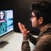 cybercrime, hacking and technology concept - male hacker with smartphone and coding on computers screen in dark room