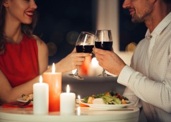 Cropped photo of young lovers having romantic dinner and drinking red wine at home