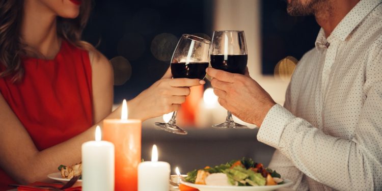 Cropped photo of young lovers having romantic dinner and drinking red wine at home