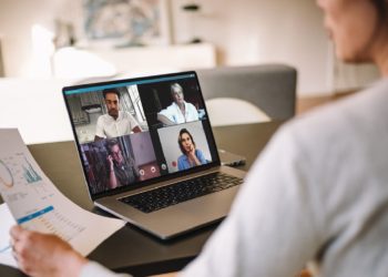 Office colleagues having a video call to discuss few financial reports. Business people working from home having a video conference. Over the shoulder view.
