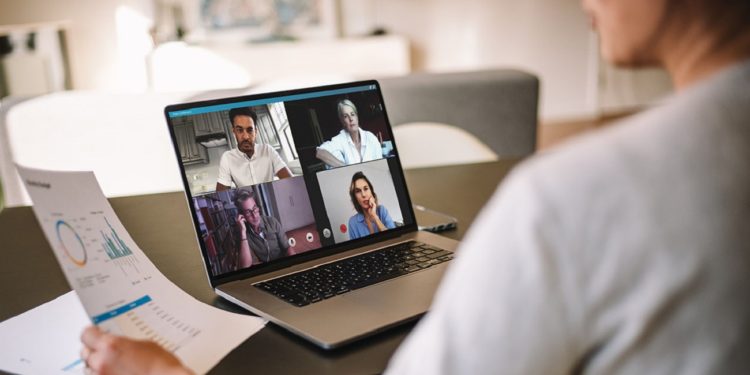 Office colleagues having a video call to discuss few financial reports. Business people working from home having a video conference. Over the shoulder view.