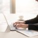 Close-up side view of serious businesswoman working at office desk on laptop, typing and looking at screen, surrounded by diagrams and calculating charts. Business, finances, economics and technology