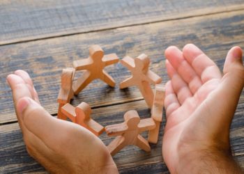 Business success concept on wooden background high angle view. hands protecting wooden figures of people.