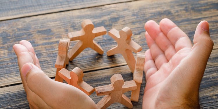 Business success concept on wooden background high angle view. hands protecting wooden figures of people.