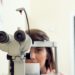 Portrait of cute caucasian female patient sitting in optometrist office, waiting for start of procedure to check her vision with microbioscope, sitting over yellow background. Ophthalmology concept.