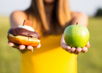 Woman choosing between healthy fruits and donut. Healthy lifestyle or nutrition concept