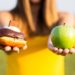 Woman choosing between healthy fruits and donut. Healthy lifestyle or nutrition concept