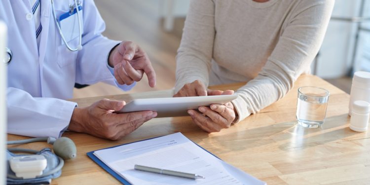 Close-up shot of unrecognizable doctor using digital tablet and discussing records with female patient