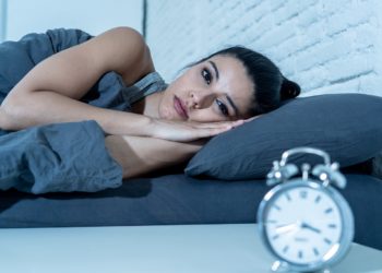 Sleepless and desperate beautiful latin woman awake at night not able to sleep looking at clock suffering from insomnia in sleep disorder concept.