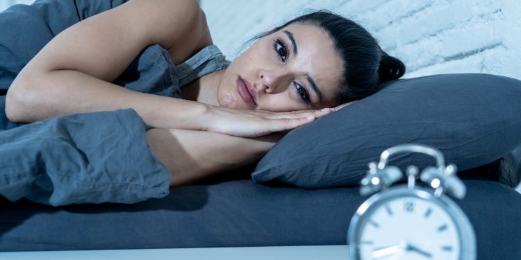 Sleepless and desperate beautiful latin woman awake at night not able to sleep looking at clock suffering from insomnia in sleep disorder concept.