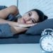 Sleepless and desperate beautiful latin woman awake at night not able to sleep looking at clock suffering from insomnia in sleep disorder concept.
