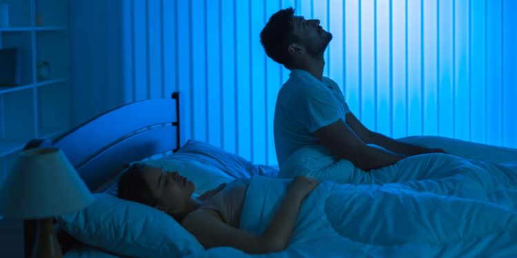 The man sit on the bed with an insomnia near woman. night time