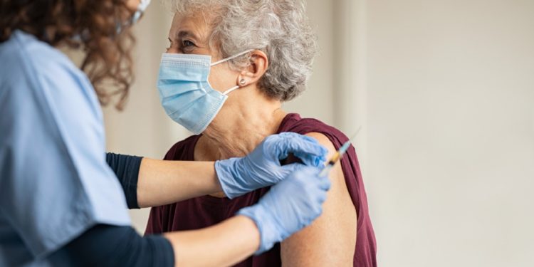 General practitioner vaccinating old patient in private clinic with copy space. Doctor giving injection to senior woman at hospital. Nurse holding syringe and using cotton before make Covid-19 or coronavirus vaccine.