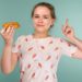Portrait of pimply teen girl wants to eat eclair cake on blue background