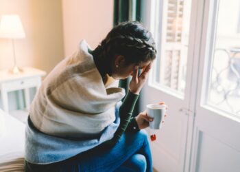 Woman with temperature staying home wrapped in scarf and drinking hot tea