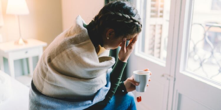 Woman with temperature staying home wrapped in scarf and drinking hot tea