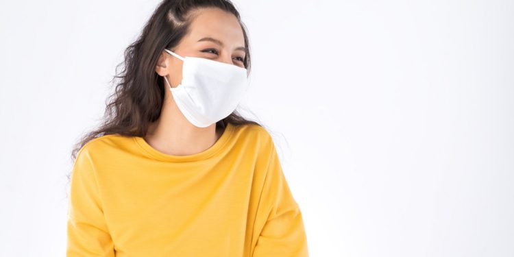 Young happy Asian woman wearing hygienic mask to prevent infection corona virus Air pollution pm2.5 she wearing a yellow sweater shoot in shot isolated on white background