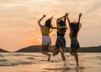 Group of three Asian young women jumping on beach, friends happy relax having fun playing on beach near sea when sunset in evening. Lifestyle friends travel holiday vacation on beach summer concept.