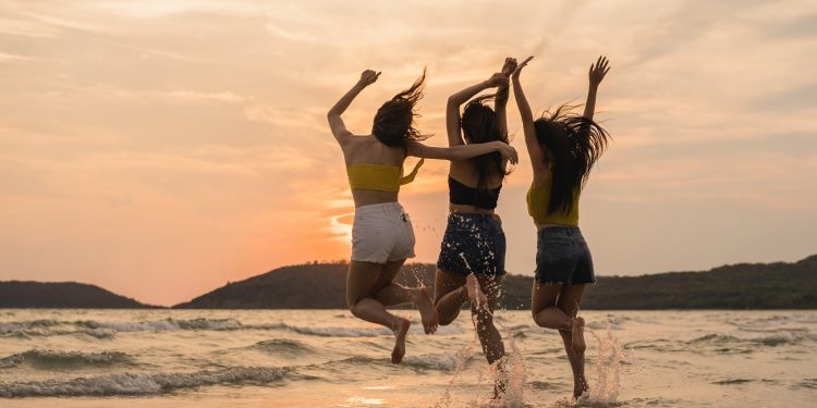 Group of three Asian young women jumping on beach, friends happy relax having fun playing on beach near sea when sunset in evening. Lifestyle friends travel holiday vacation on beach summer concept.