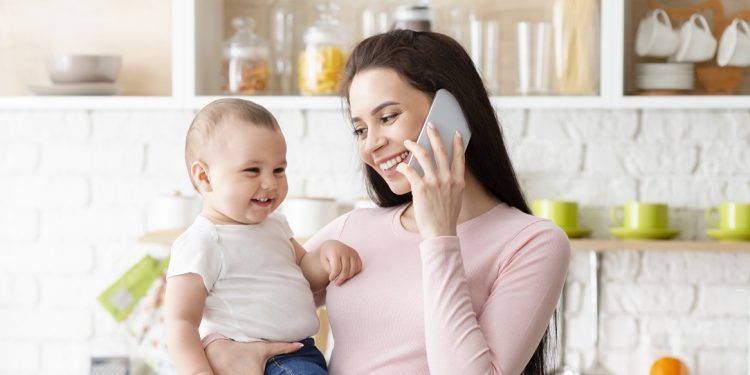 Happy motherhood. Cheerful mom bonding with baby and talking on cellphone, panorama