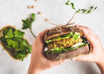 Vegan sandwich with chickpea patty, avocado, cucumber and greens in rye bread in children's hands, top view.