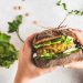 Vegan sandwich with chickpea patty, avocado, cucumber and greens in rye bread in children's hands, top view.